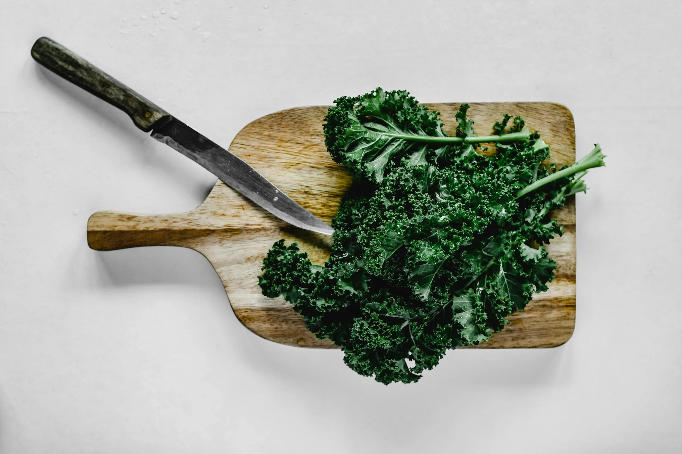 Kale on a wooden cutting board with metal knife next to it. Below is the white background.