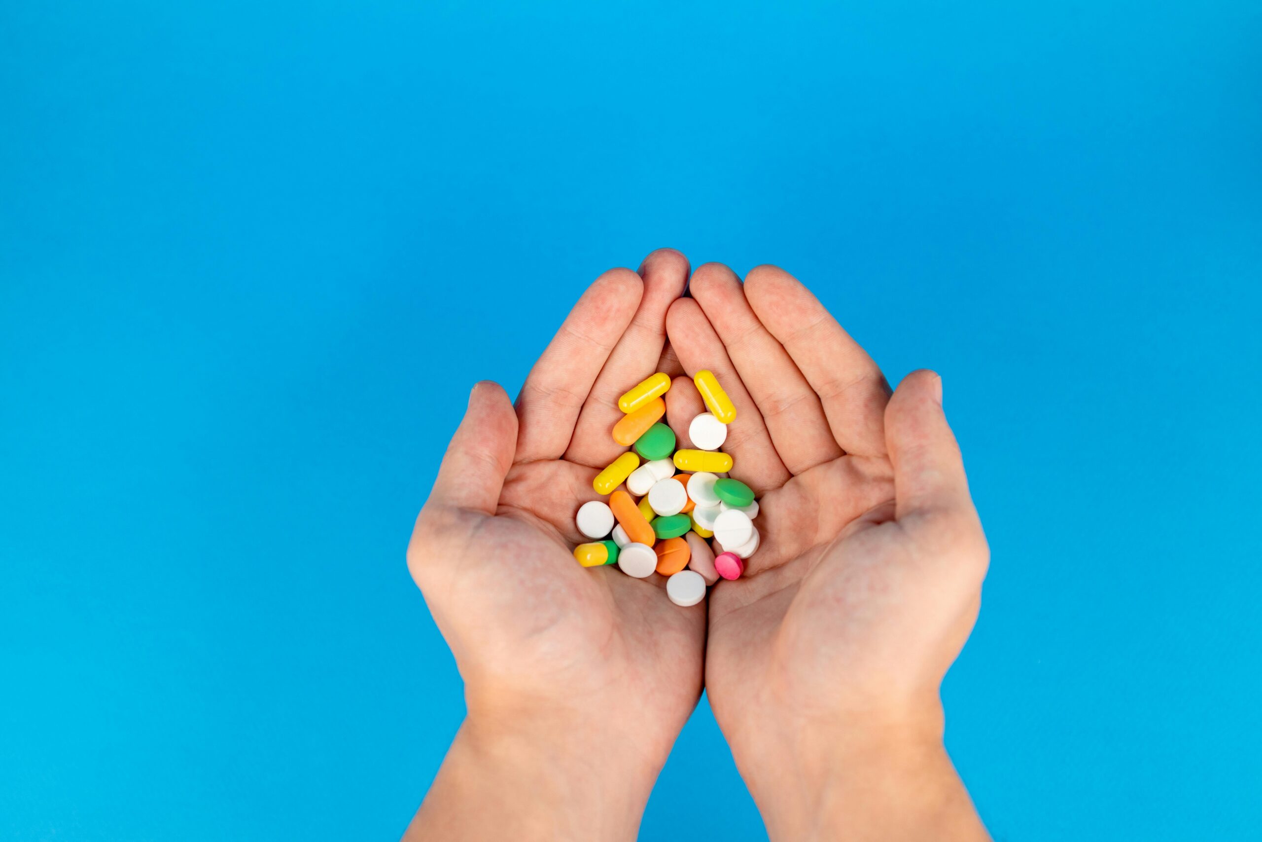 Hands holding colorful medicines, background is light blue.