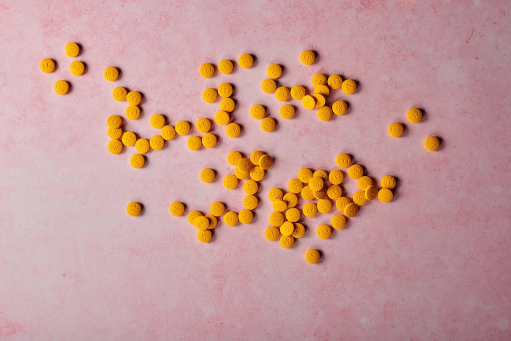 Many yellow pills on a rose surface.